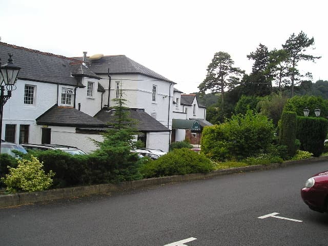 A white country house hotel behind shrubs and a car park