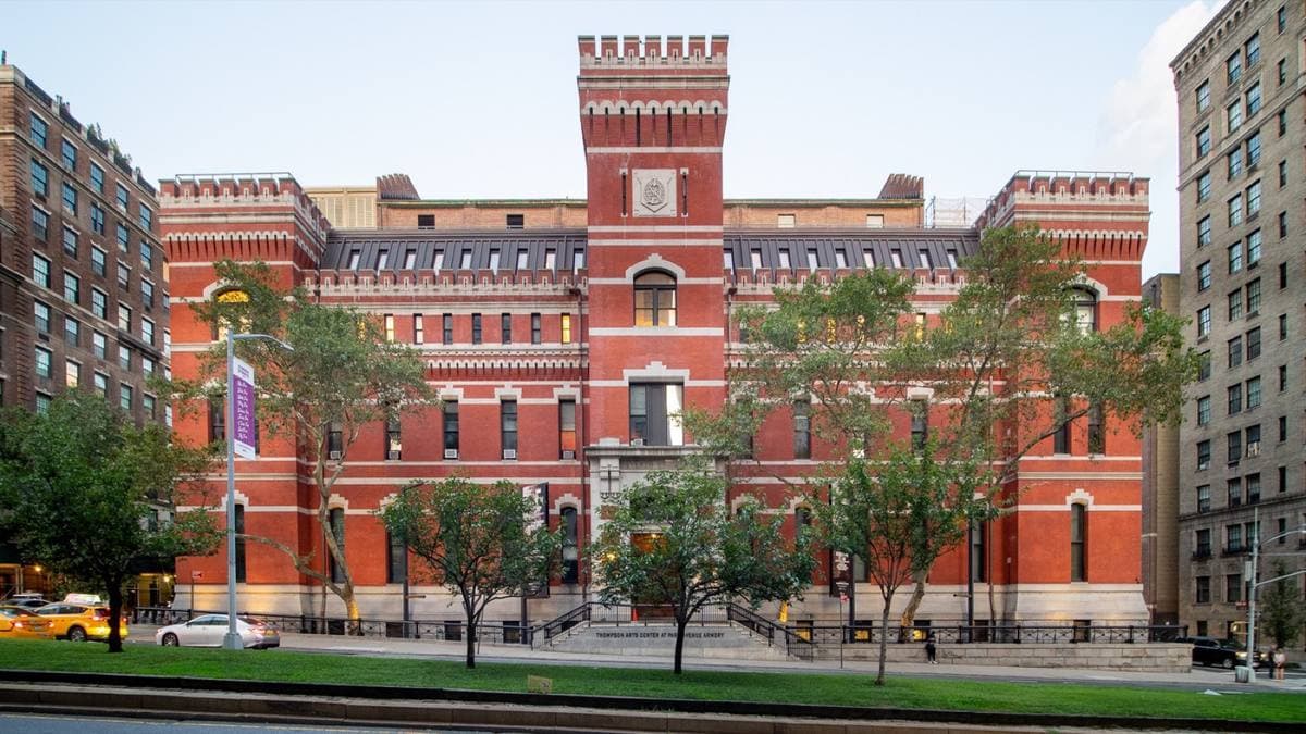 A long red-brick armory with crenellated towers behind trees