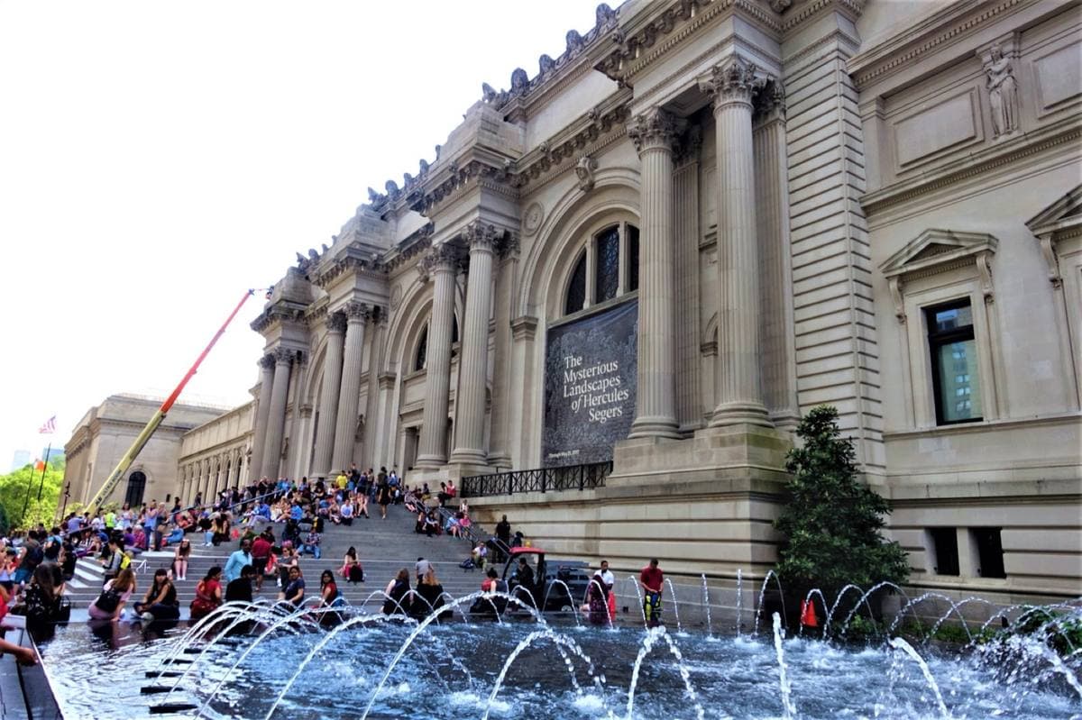 Crowds sitting on the wide stone steps of the Metropolitan Museum, fountains in front