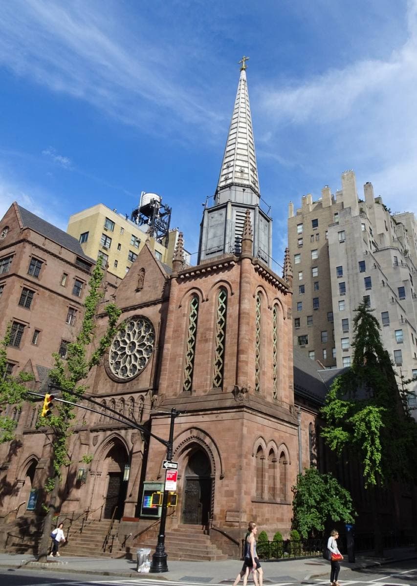 A brownstone Gothic church with a tall spire on a street corner