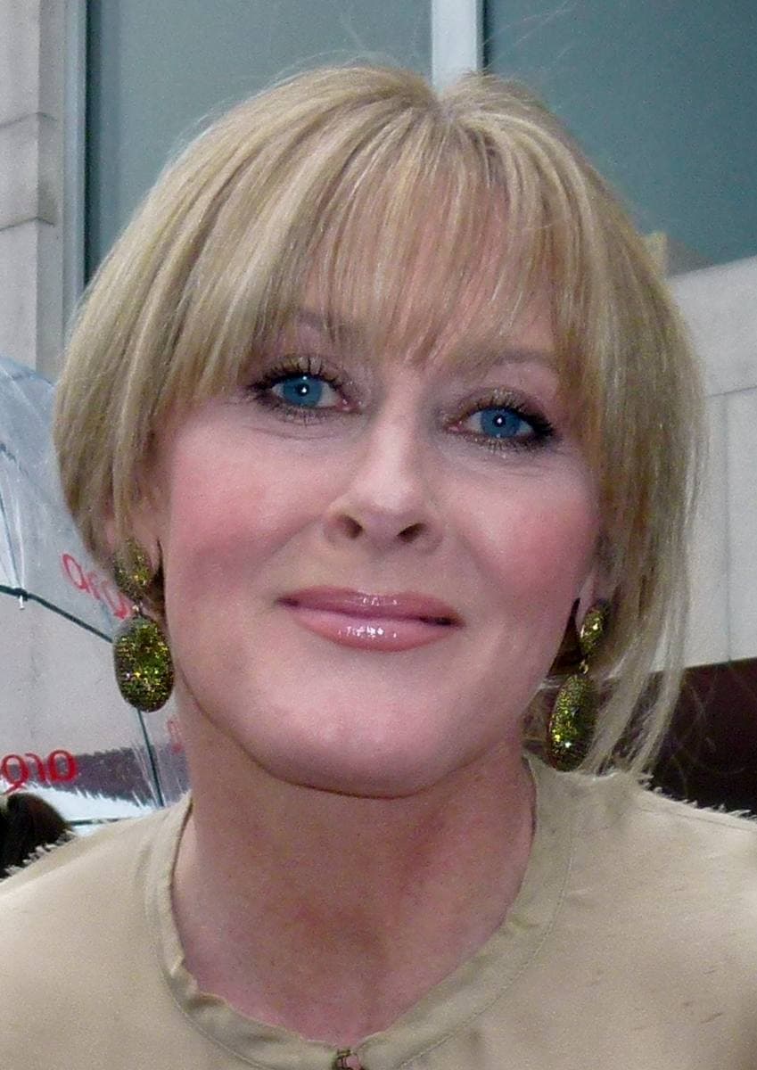 Sarah Lancashire with a blonde fringe and large gold earrings, smiling