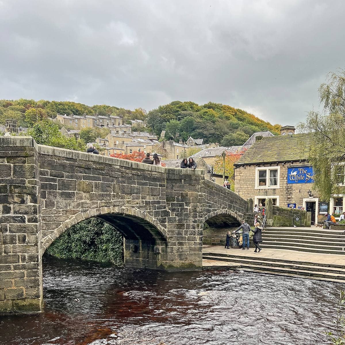 A humped stone arch bridge over a brown river, with stone buildings beyond