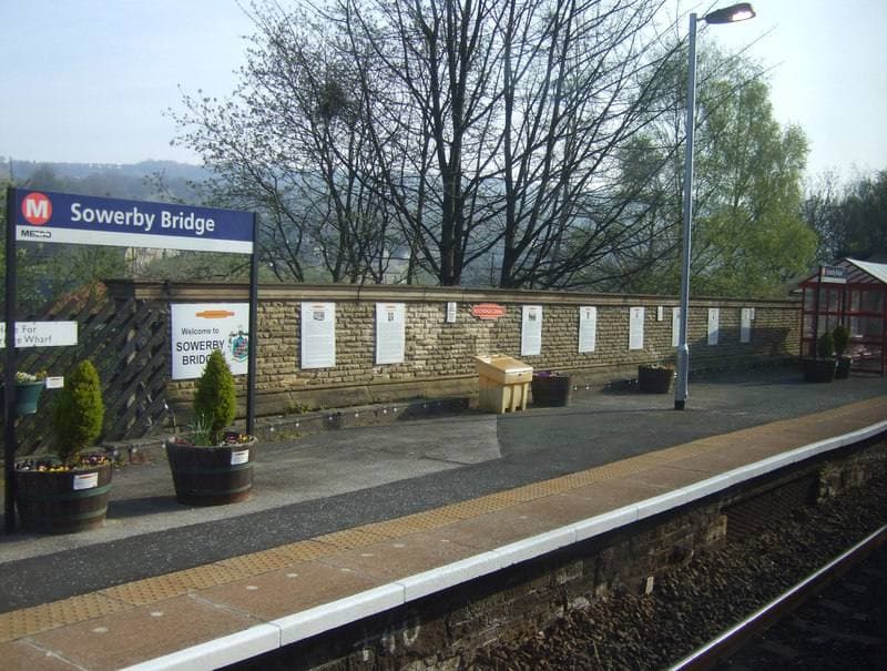 A station platform with a Sowerby Bridge sign, planters and a stone wall