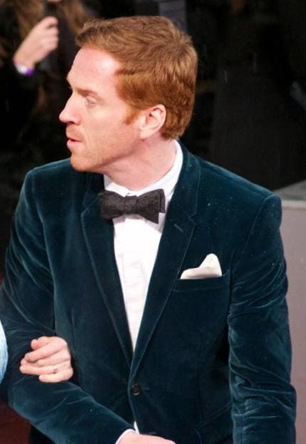 Damian Lewis with red hair, in a dark green velvet dinner jacket and bow tie
