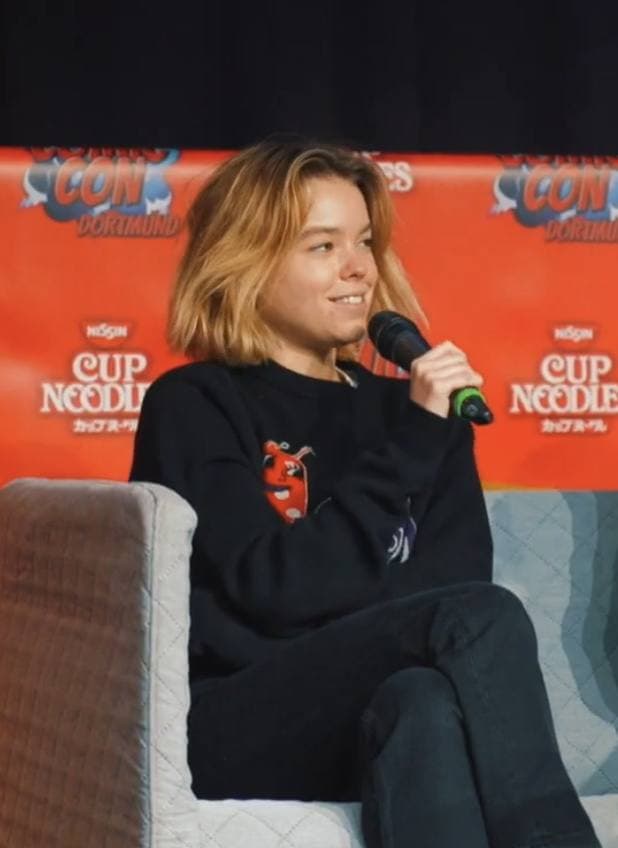 A young woman with long fair hair smiling on a convention stage