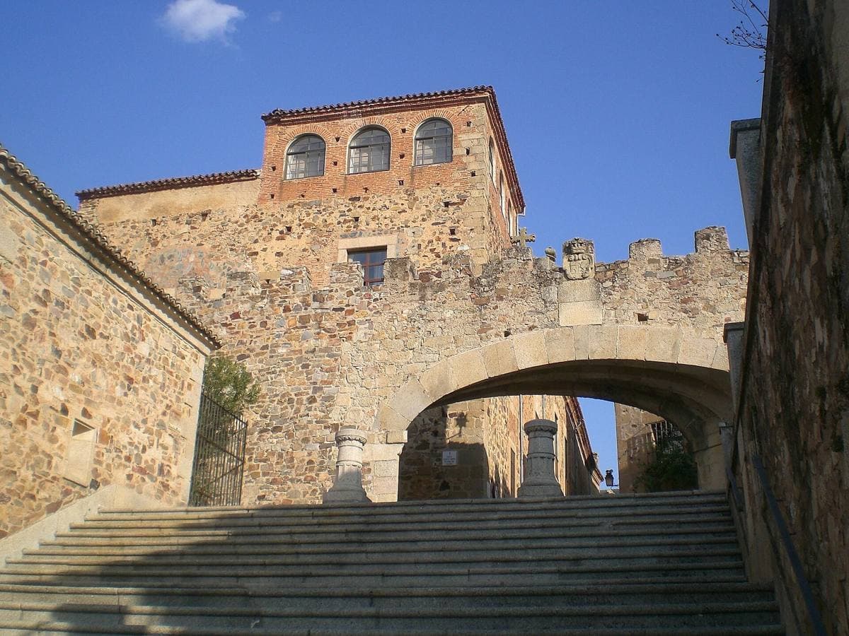 A wide stone archway in a medieval wall with a tower above it