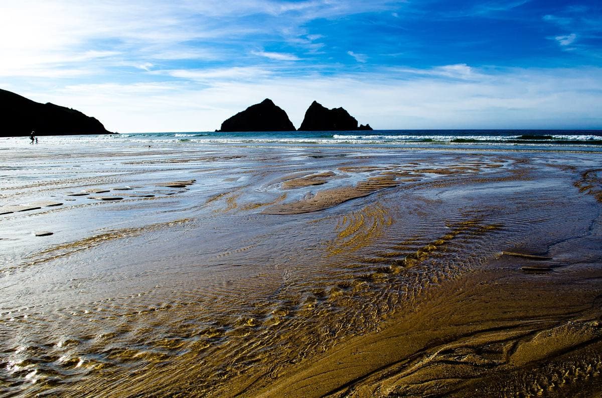 Wet rippled sand at low tide with two dark rock islands on the horizon