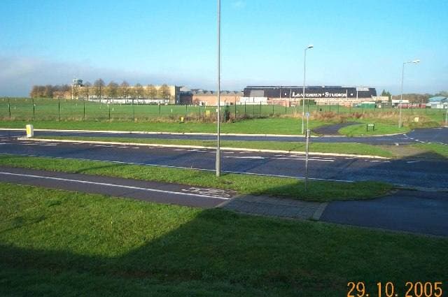 Large pale studio sheds behind a fence and grass verge