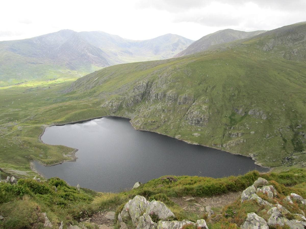 A dark mountain lake in a bowl of steep grassy and rocky slopes