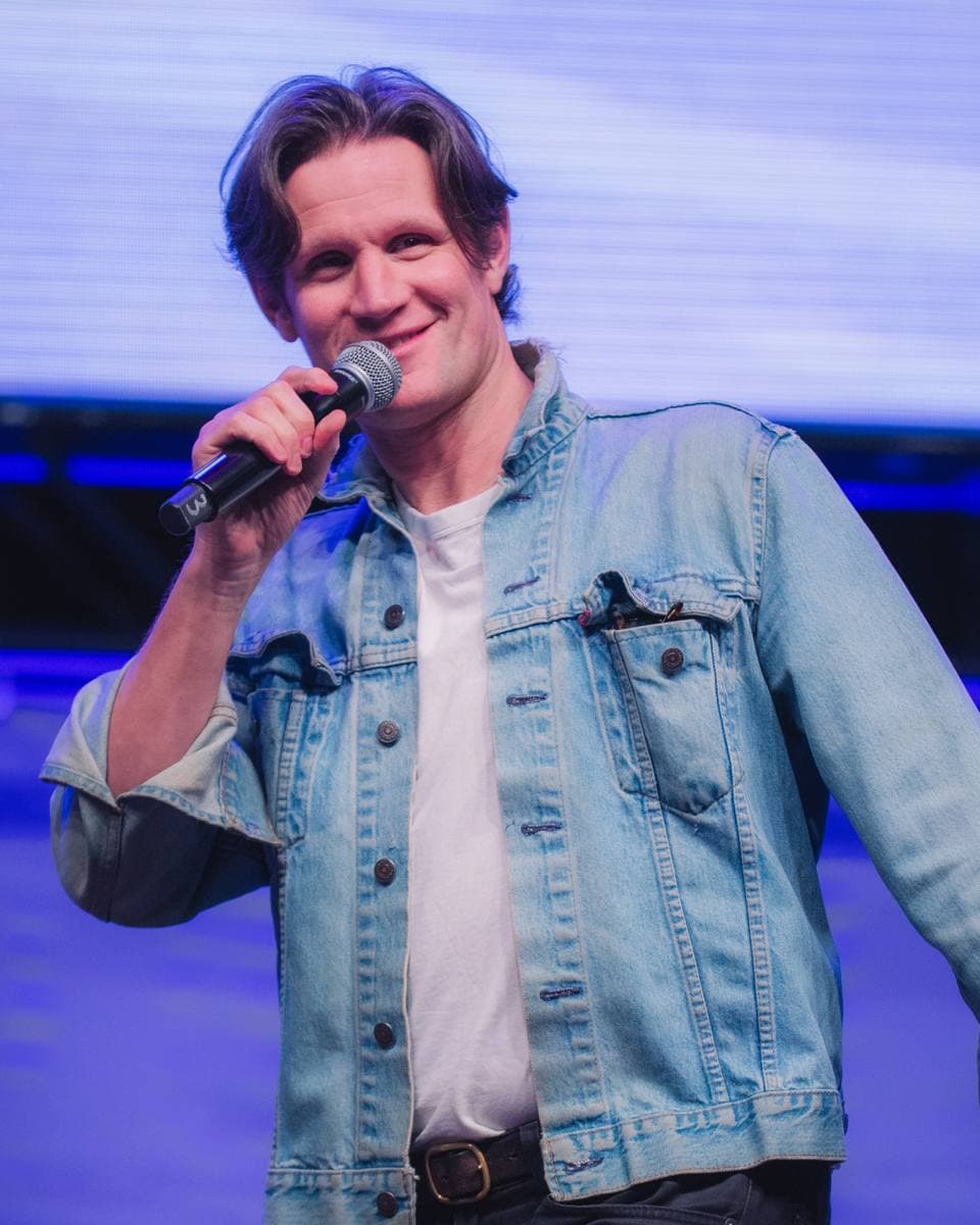A man with dark swept-back hair speaking into a microphone