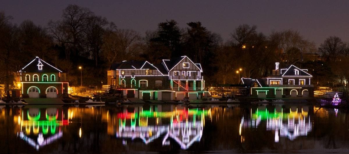 A row of boathouses outlined in lights reflected in the river