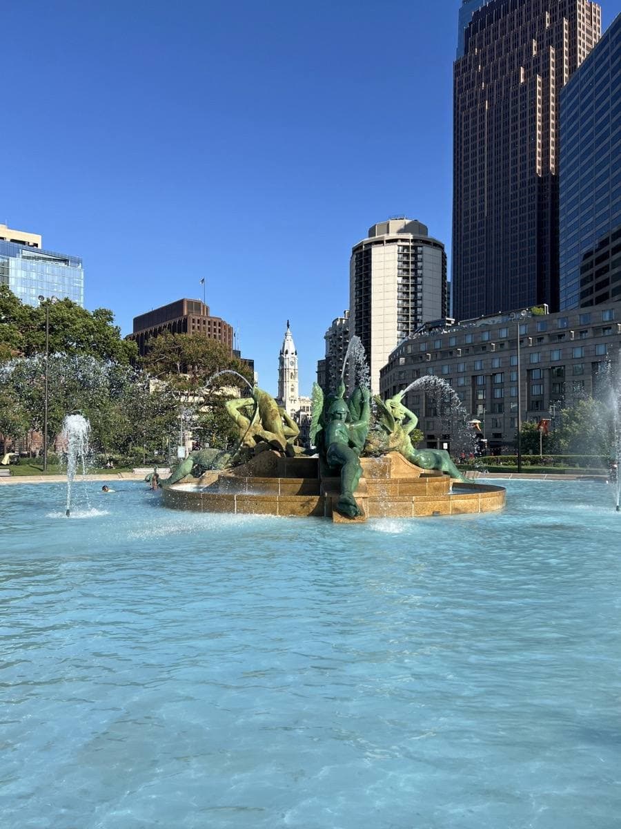 Fountain jets and bronze figures in a circular basin with trees behind
