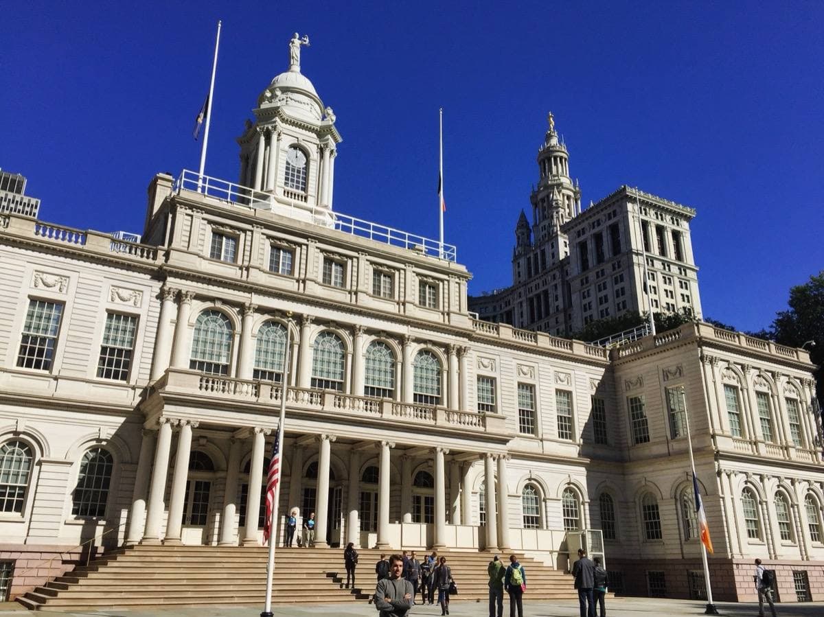 The pale stone front of New York City Hall with its steps and cupola