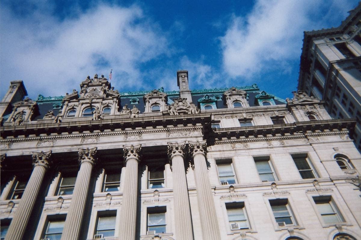 A grey Beaux-Arts building with columns and sculpture along Chambers Street