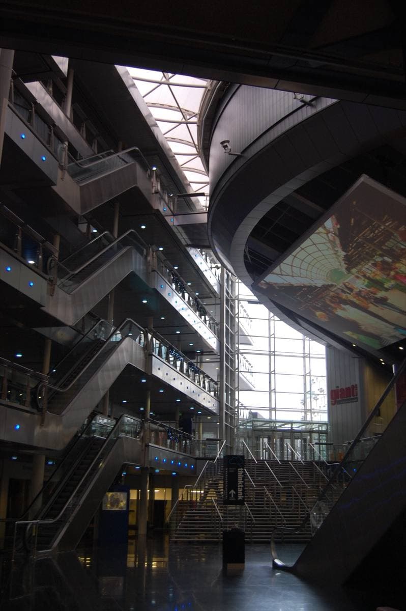A tall glass atrium with escalators and walkways crossing several floors