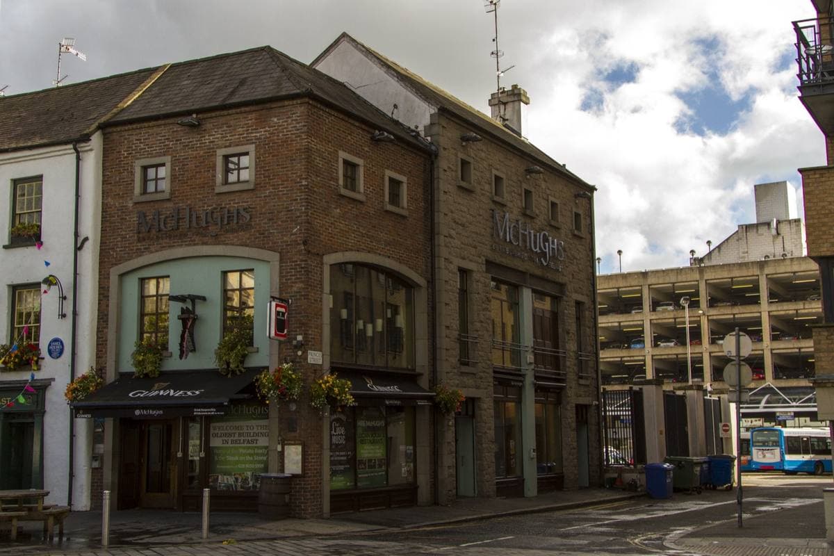 A low old pub front with a painted sign beside taller later buildings