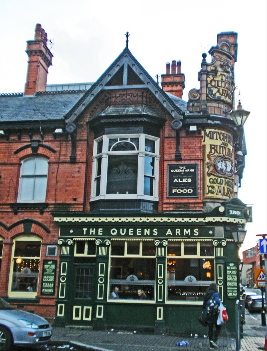 A red-brick Victorian corner pub with tiled lettering and lit windows