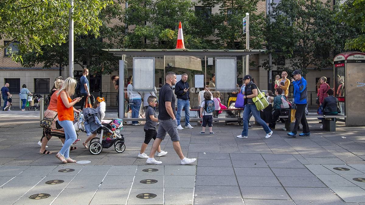 People walking across a paved city square with trees and a bus shelter