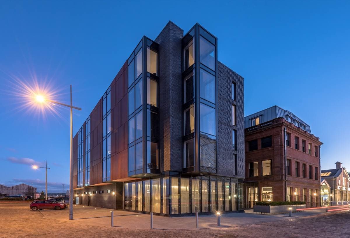 A red-brick Edwardian office building with tall windows, lit at dusk