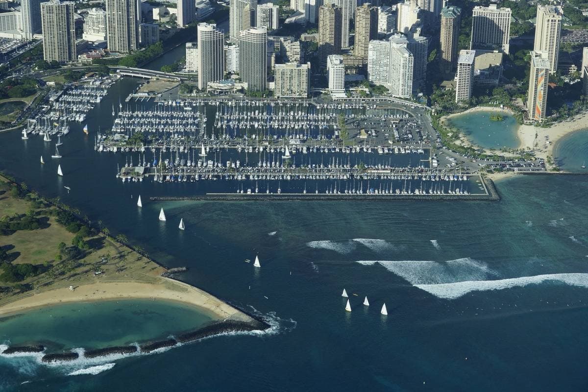 Rows of yachts in a marina beside Waikīkī high-rises, seen from the air