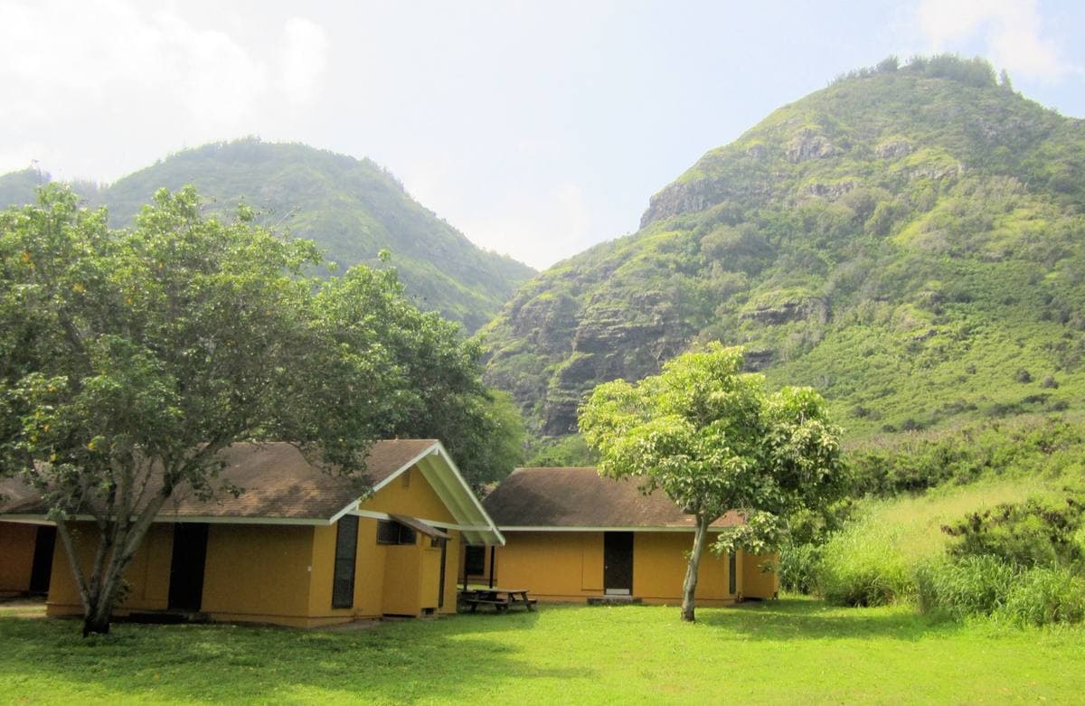 Mustard-yellow single-storey cabins on a lawn below steep green ridges