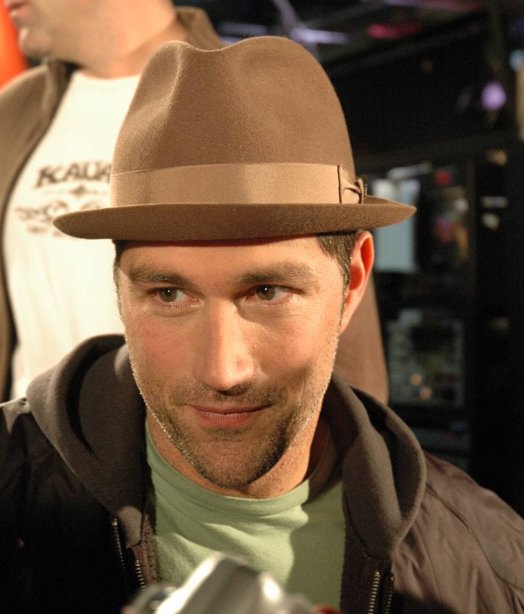 Matthew Fox in a brown trilby and dark jacket, smiling slightly