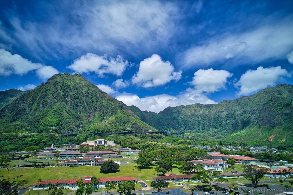 Low campus buildings on a plain beneath a steep green peak