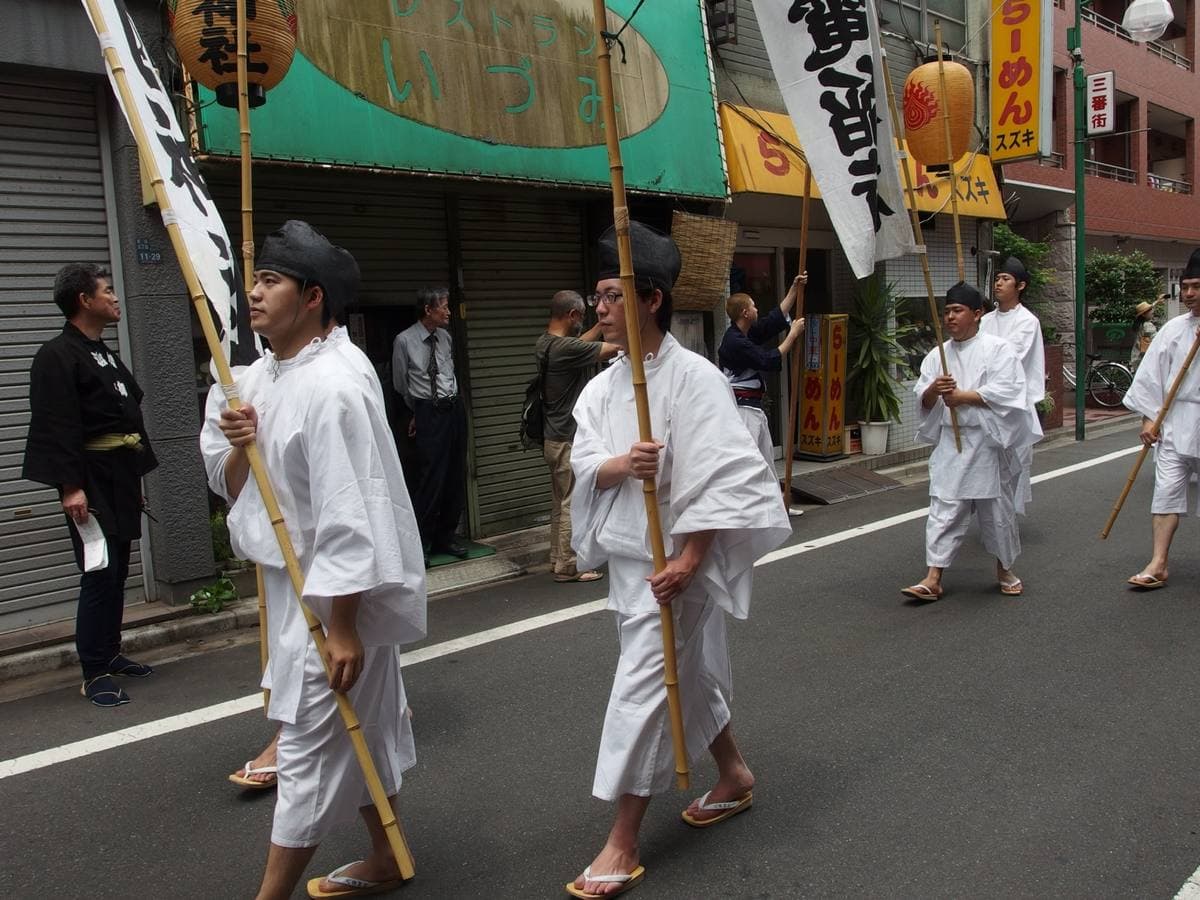 Men in white robes carrying banner poles through a Shinjuku street during the shrine festival