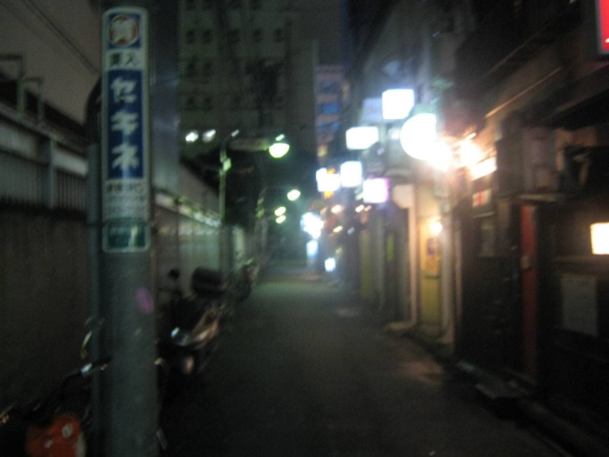 A dark Golden Gai lane in 2009, a street-name pole on the left and small lit bars running away into the distance