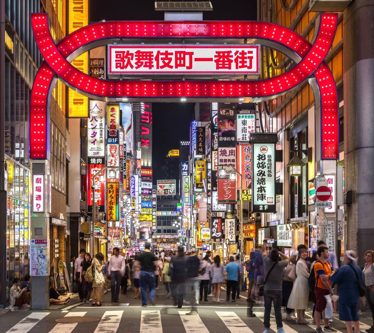 The red lit arch of Kabukicho Ichibangai over a crowded street of neon signs at night