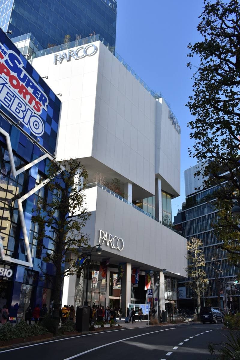 The white facade of Shibuya PARCO on a sunny day, with trees along the pavement