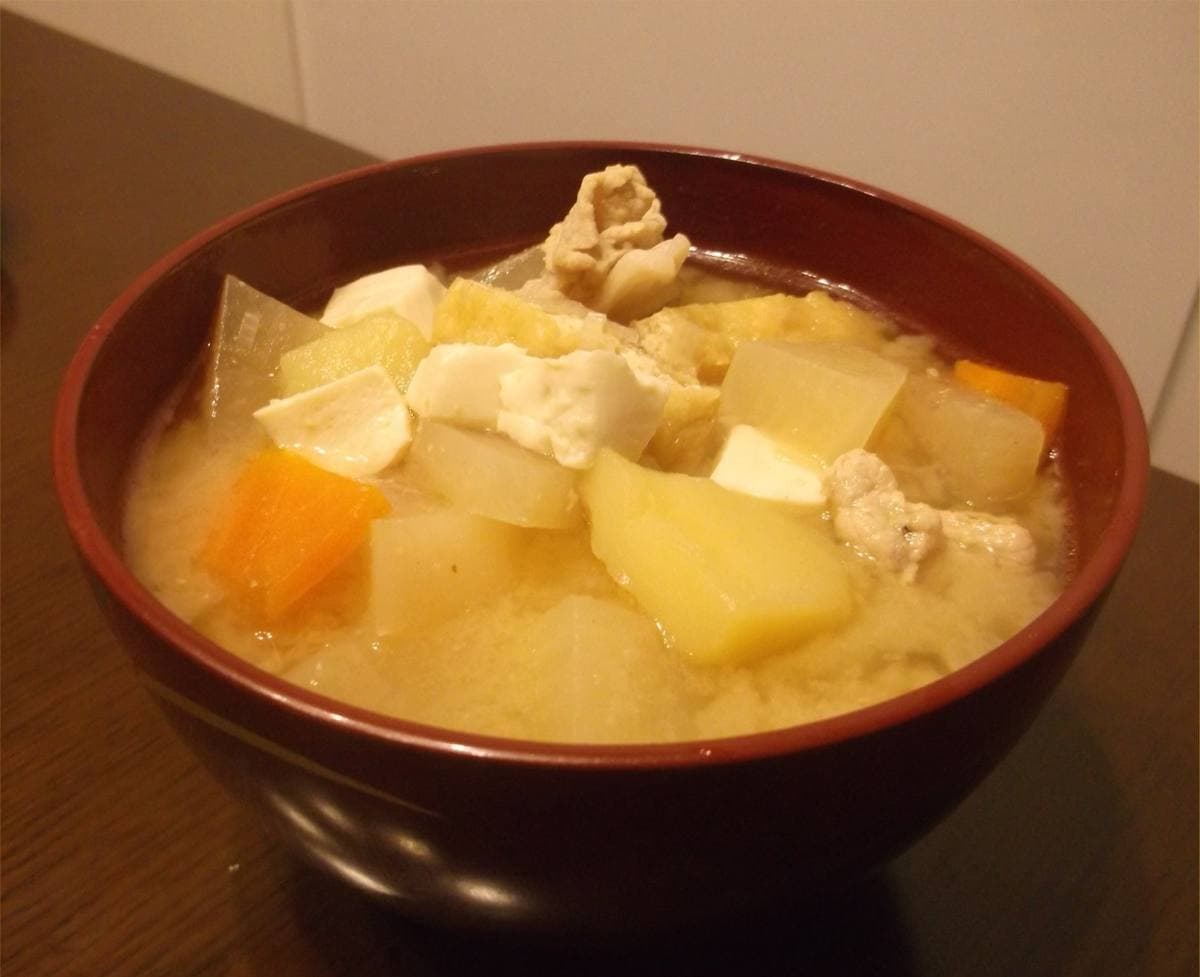 A lacquered bowl of miso soup with pork, tofu, carrot and potato