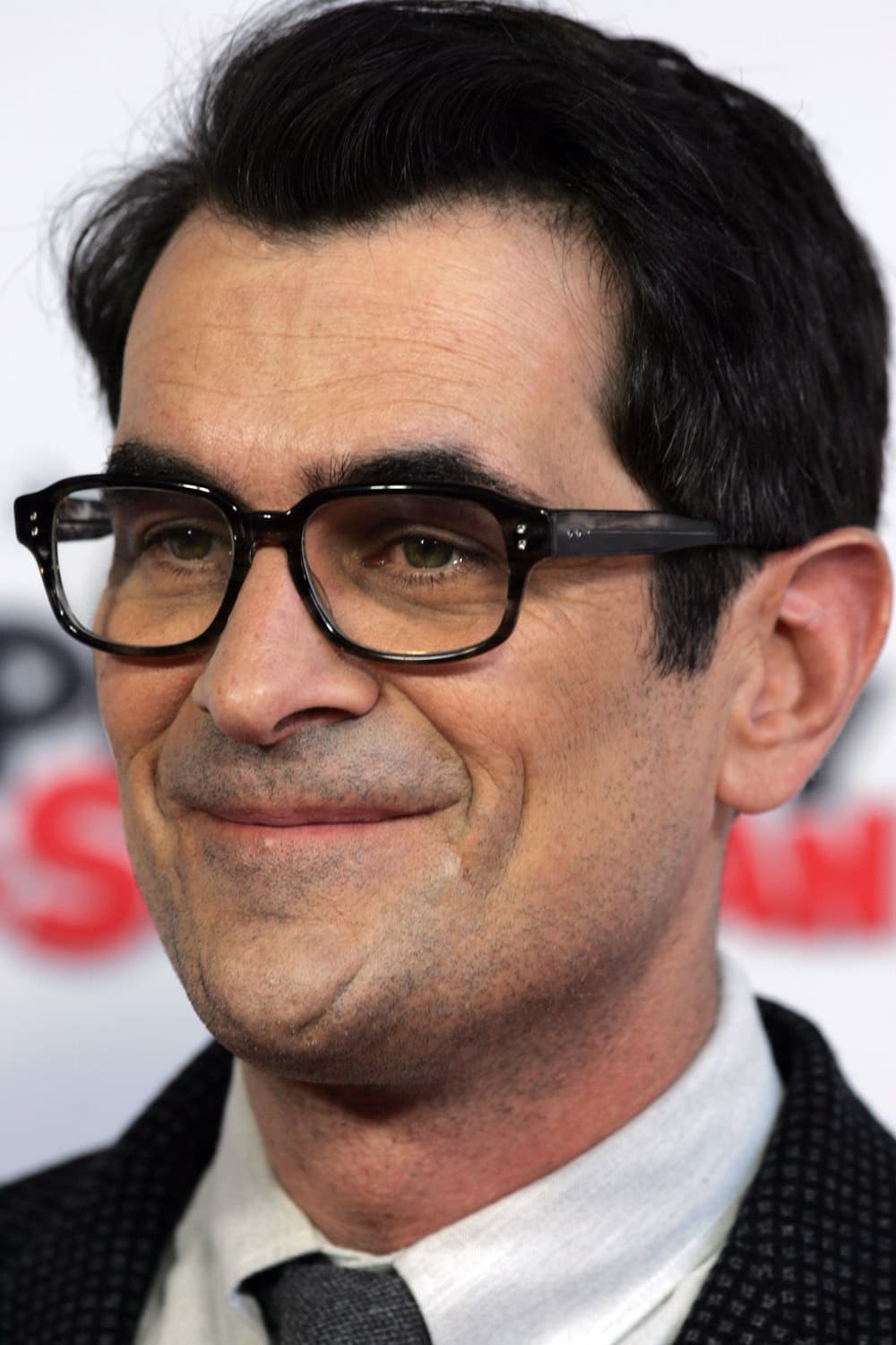 Ty Burrell in black-rimmed glasses, smiling to one side