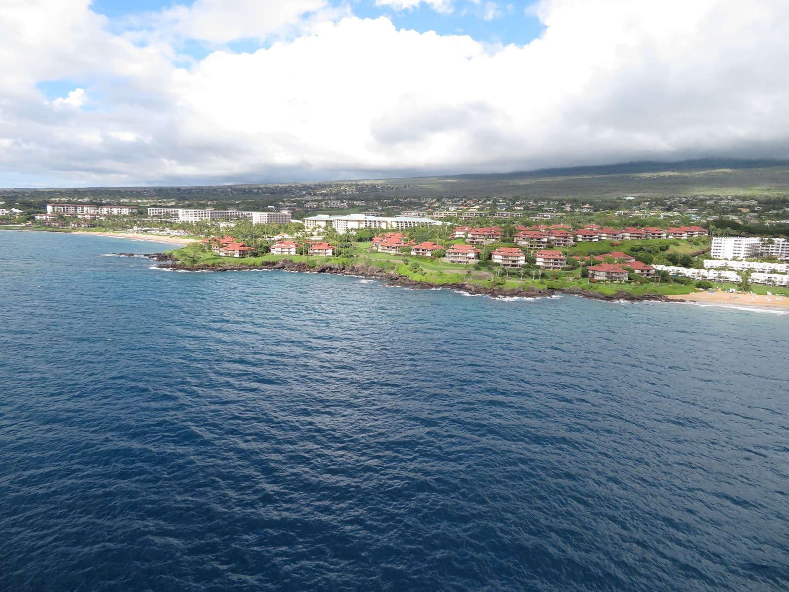 Aerial view of a green point with low resort buildings above a blue sea