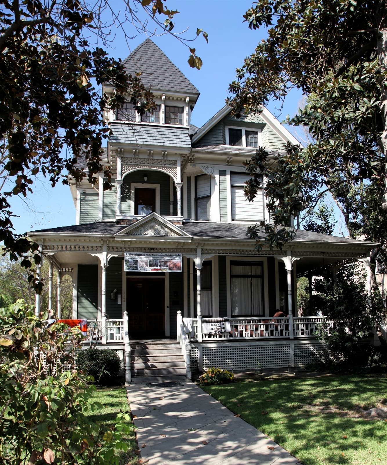 A pale Victorian house with a turret and a wide porch behind a garden path