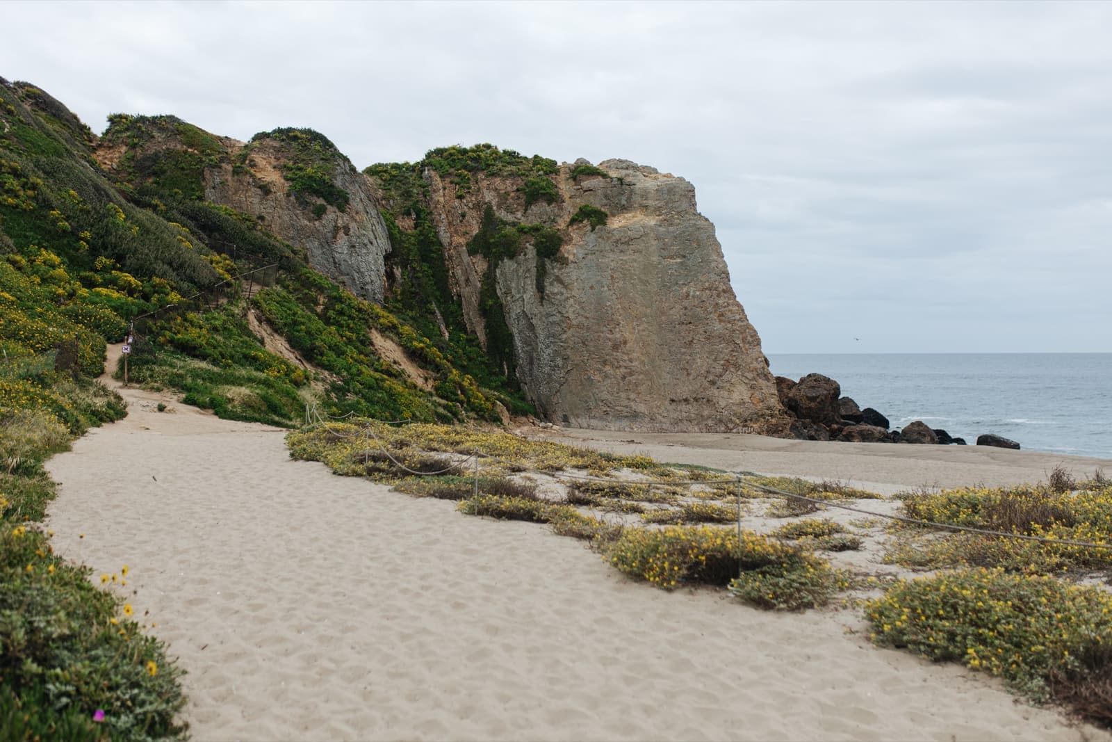 A sand path running to a tall rock headland above the sea