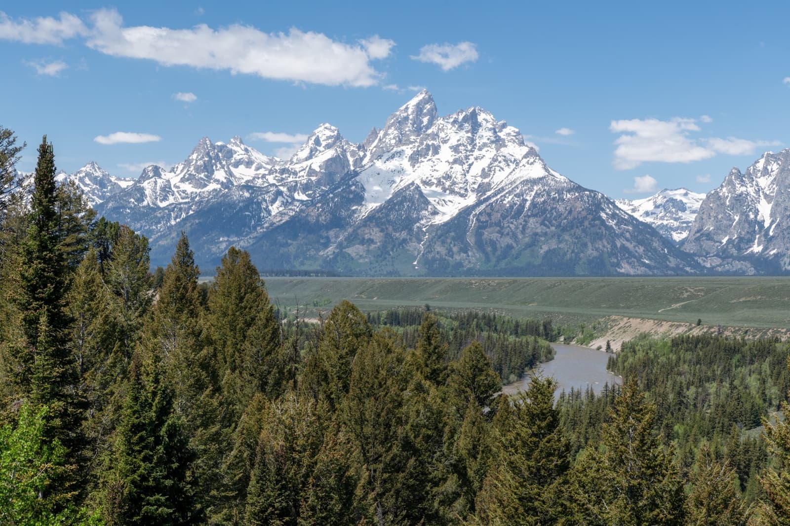 Snow-capped jagged peaks above a forested valley and a river bend