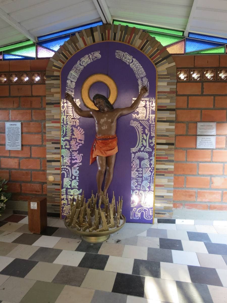 A brightly coloured memorial sculpture of a figure with arms spread, in a small brick chapel with stained glass