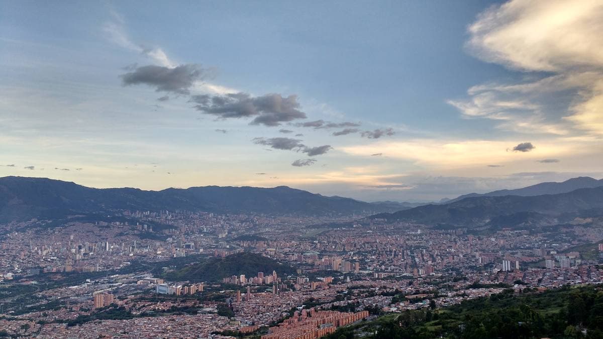 A wide valley filled with a city of brick and white towers under green mountains and a pale sky