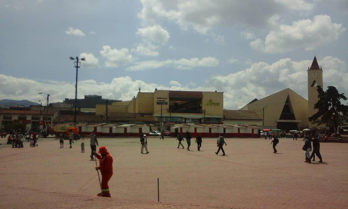A town square with trees, benches and low colonial buildings