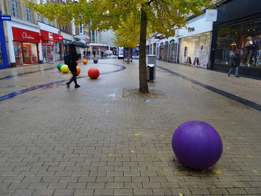 A paved shopping street with trees and large coloured balls