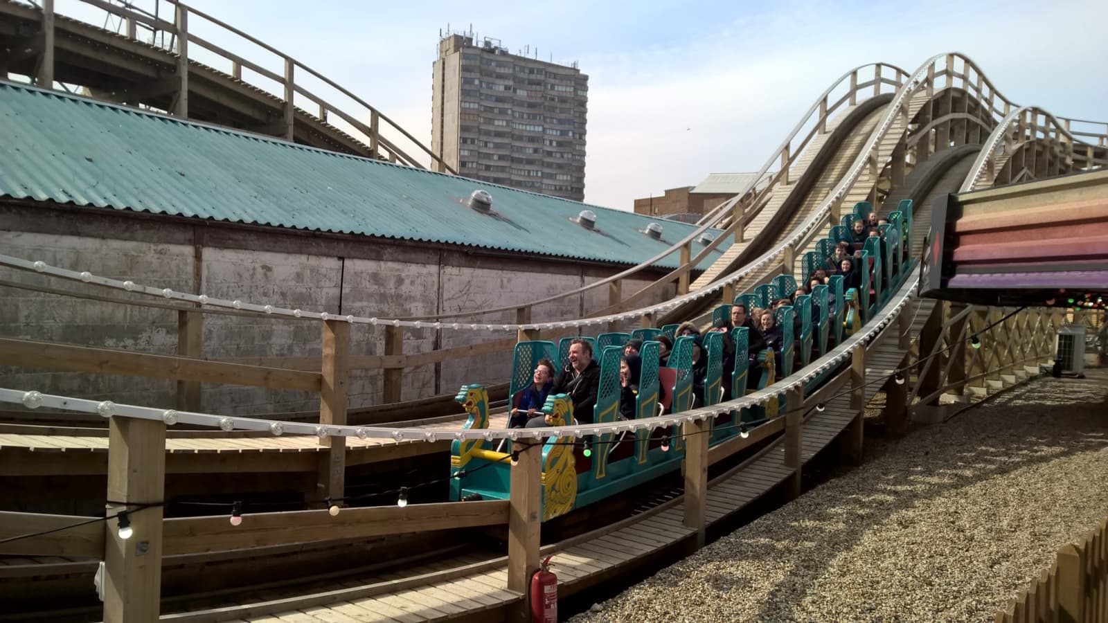 A wooden roller coaster car with green seats on its track