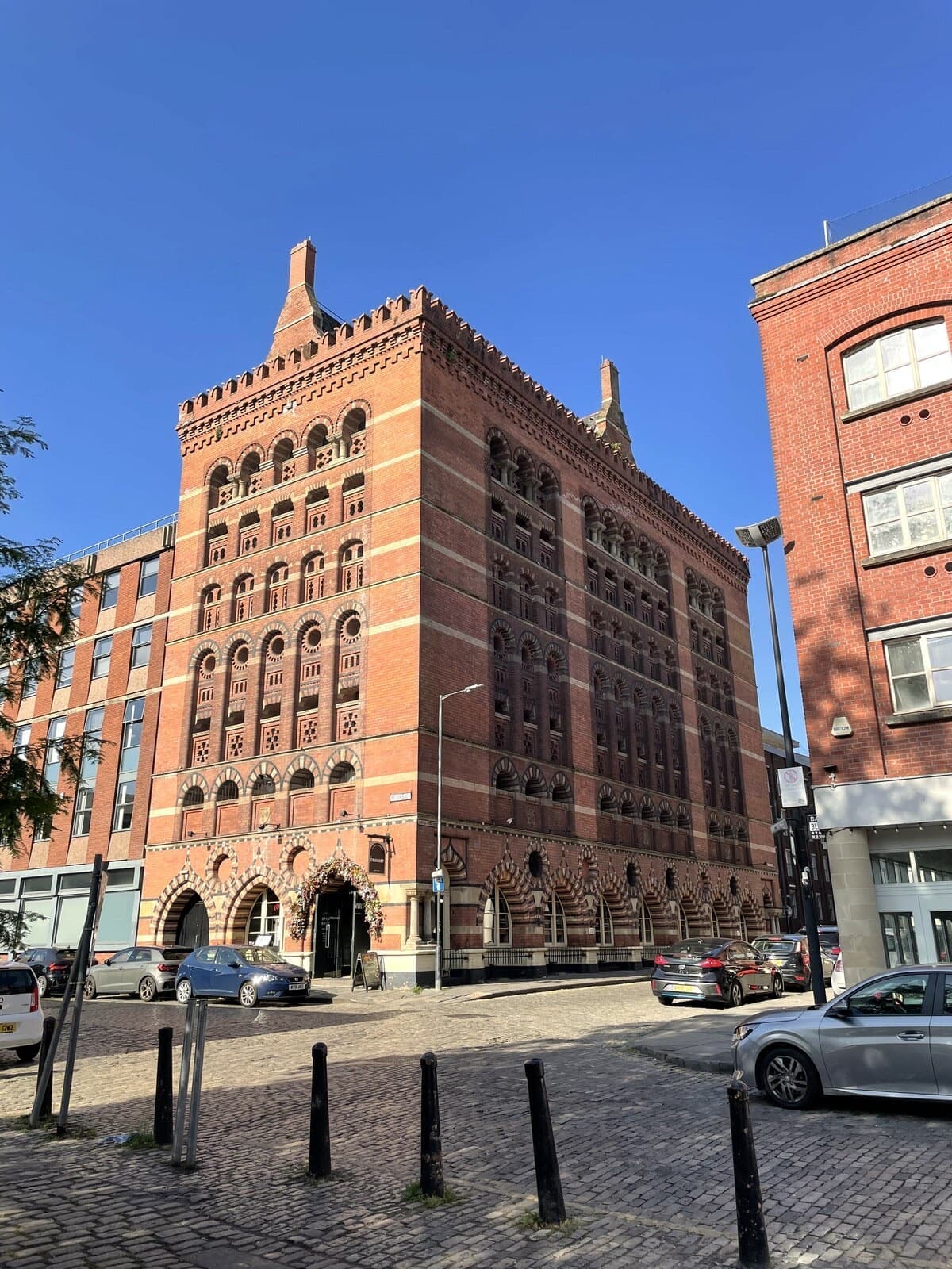 A tall red-brick Victorian granary with arched windows on a cobbled corner