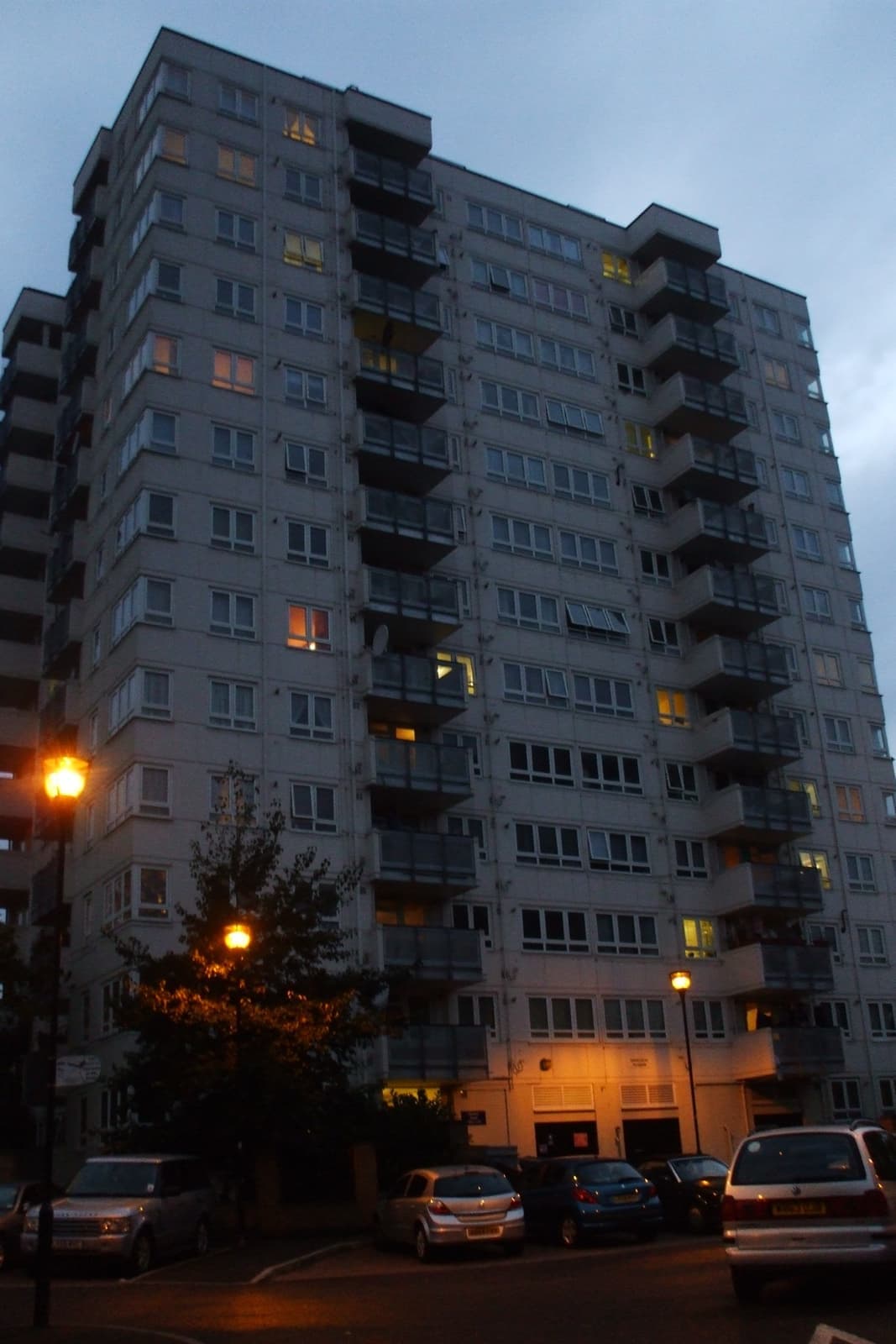 A grey concrete tower block at dusk with lit windows