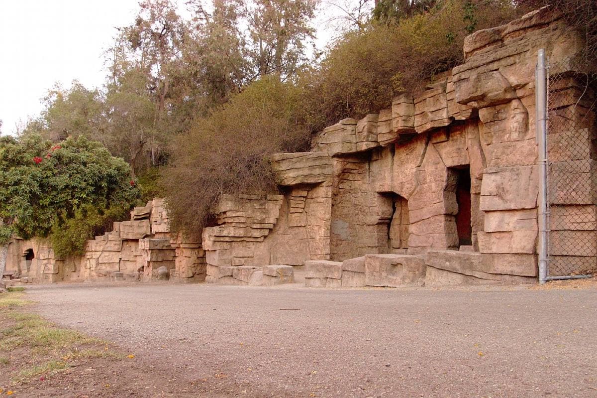Artificial rock caves with barred openings along a dirt path under trees