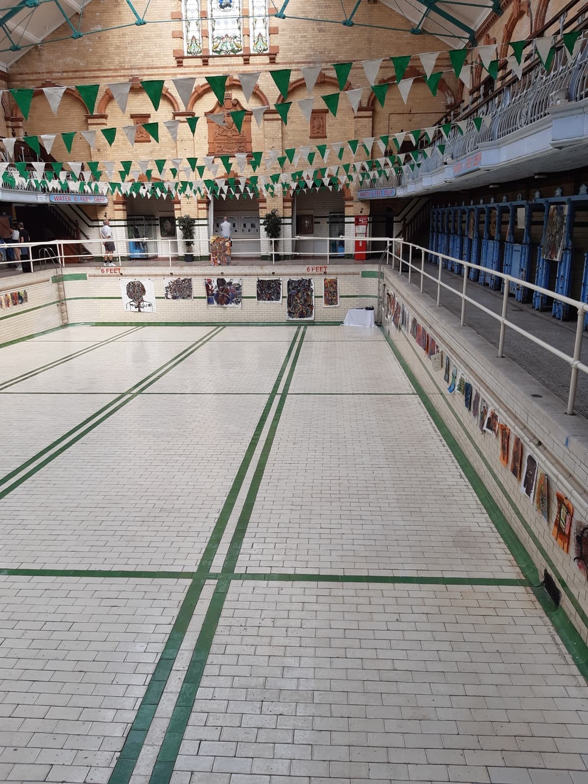 An empty tiled swimming pool under a glass roof with bunting and changing cubicles