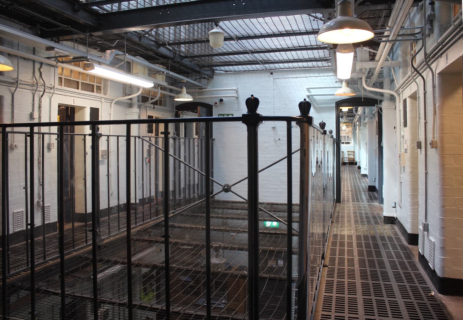 Two tiers of cell doors and iron railings along a glass-roofed gallery