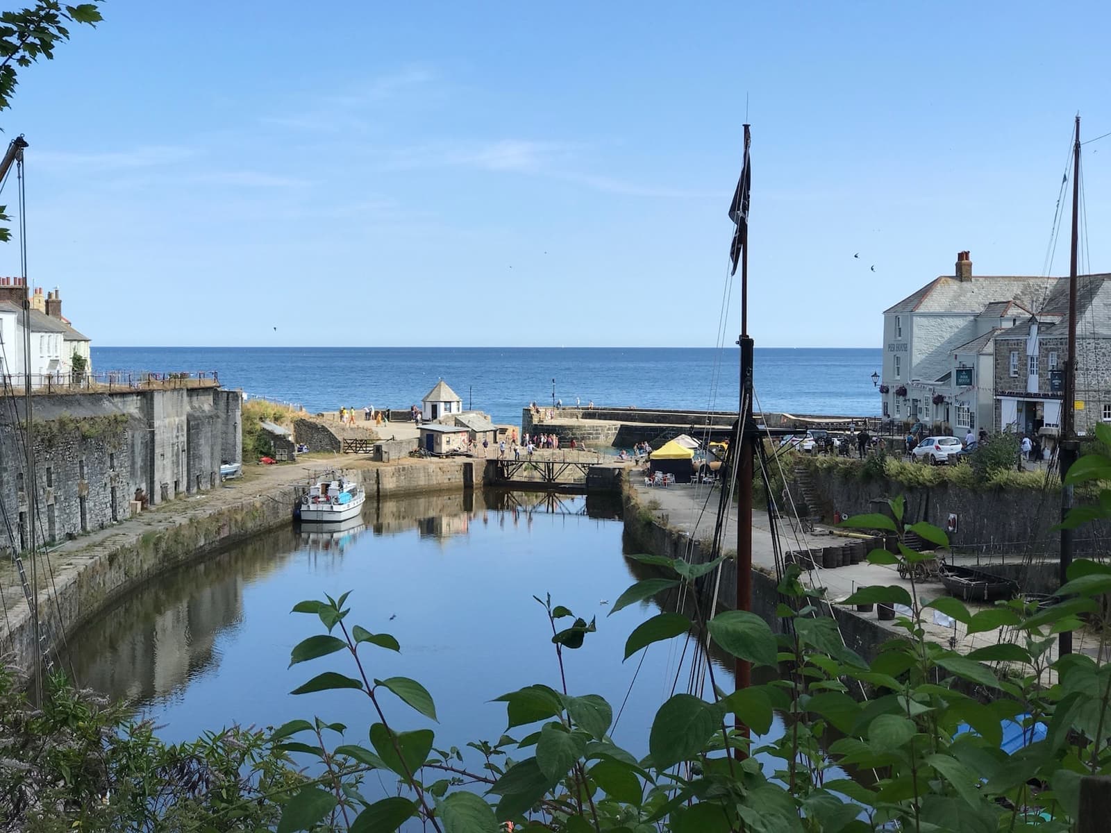 A stone-walled harbour basin with a tall ship’s masts and white Georgian houses beyond