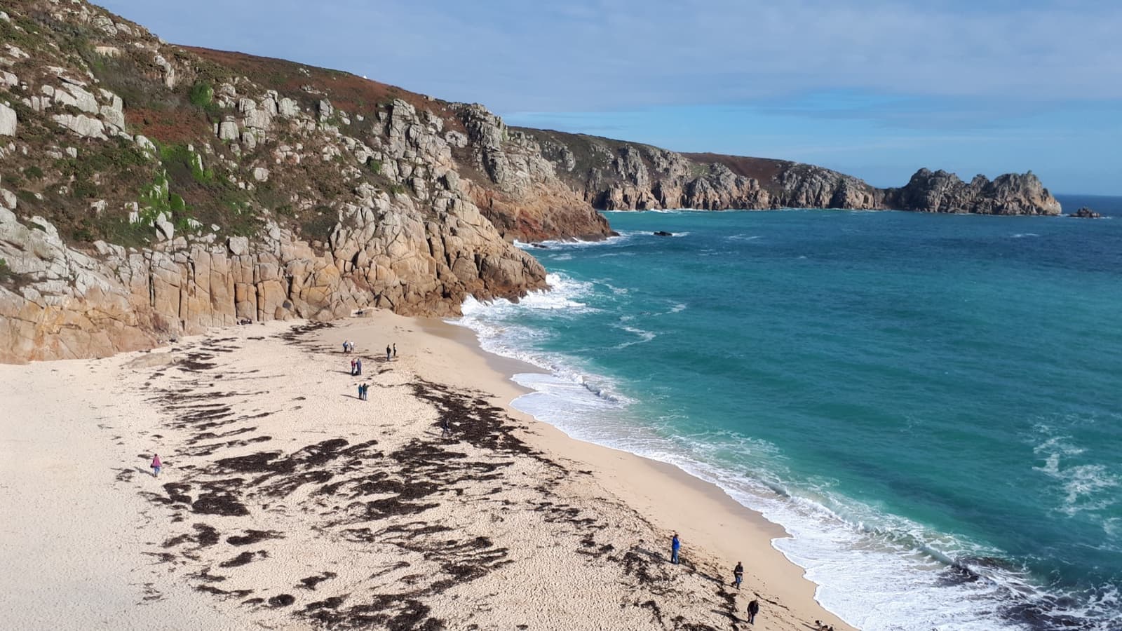 A pale sandy beach under granite cliffs with turquoise water running out to a headland