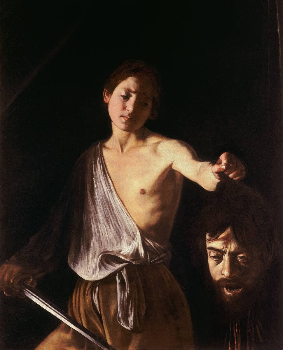 A young man emerges from darkness holding up a sword and a severed head, painted in deep shadow